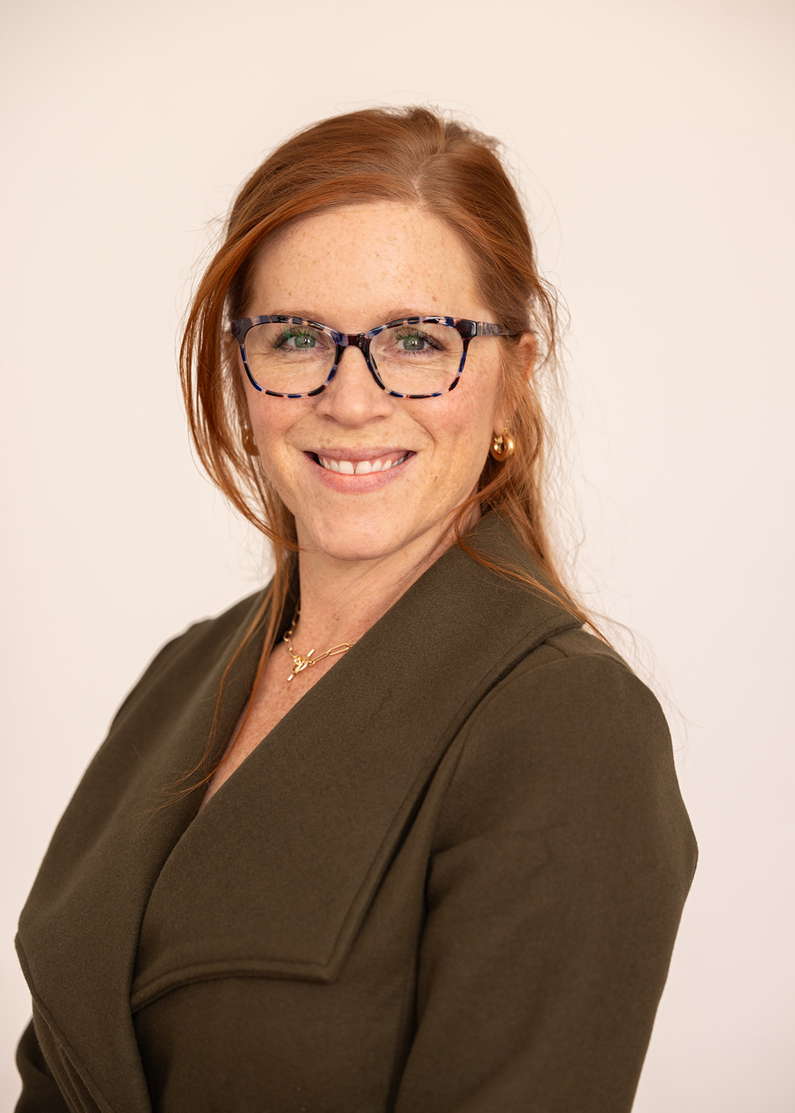 Headshot of woman wearing glasses and brown suit.