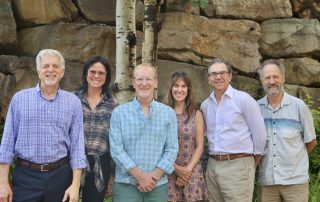 Six people standing behind a rock posing for a photo.