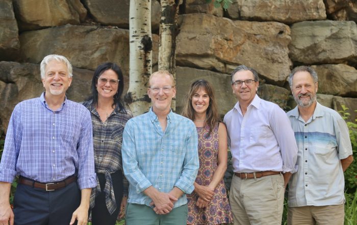 Six people standing behind a rock posing for a photo.