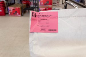 White bag in hardware store with a red tag reading "For the Birds" bird seed.