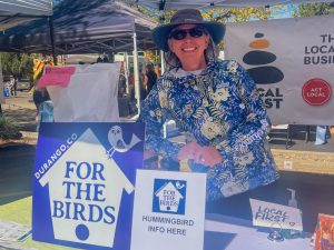 A woman leaning against a large bag of bird feed under a tent.