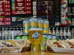 Photograph of beer cans, beer, and foods on top of a bar.