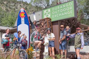 A group photo with 8 people standing in front of a sign that reads "Durango Outdoor Exchange"
